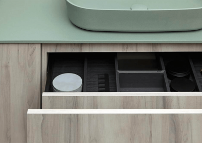 Accesorios de baño 3. Vista de mueble bajo de lavamanos con cajones abiertos de textura y color madera, encimera de color verde.