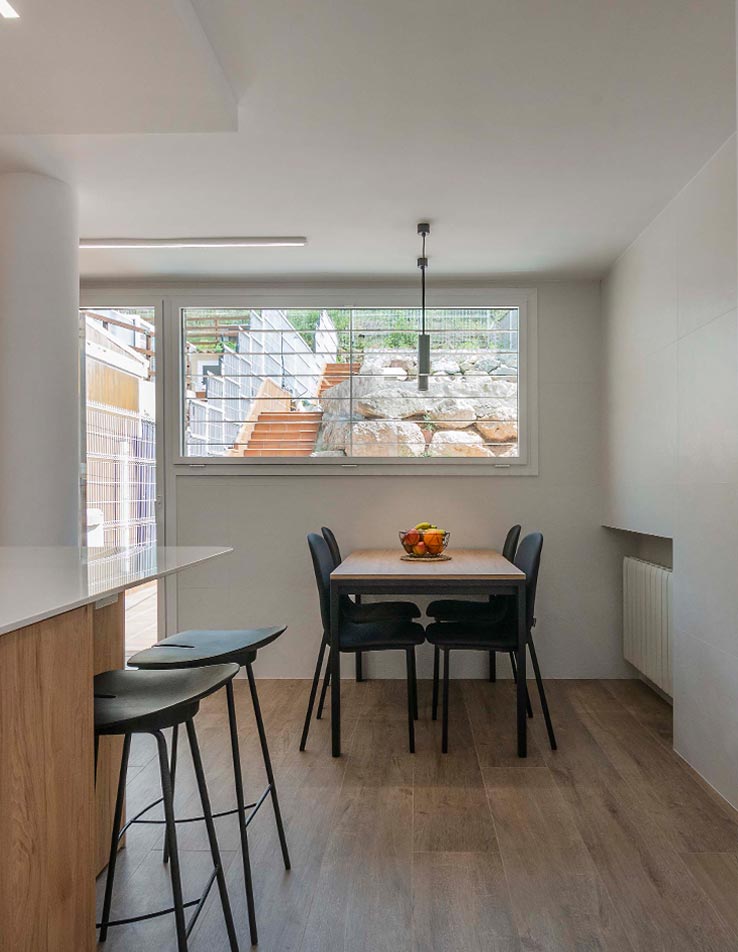 Vista de la cocina comedor de una vivienda remodelada por Vibel Estudi. Paredes blancas que contrastan con el parquet y los muebles bajos de la cocina en color y textura de madera.